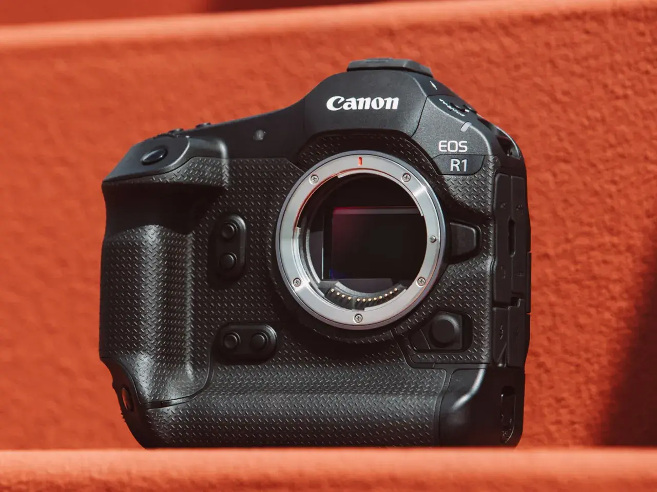 Profesjonalny aparat Canon EOS R1 z obiektywem na pomarańczowym tle.