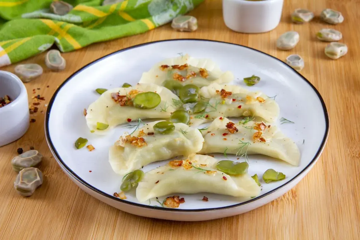 Pyszne pierogi z bobem, posypane skwarkami i koperkiem, prezentują się apetycznie na talerzu.