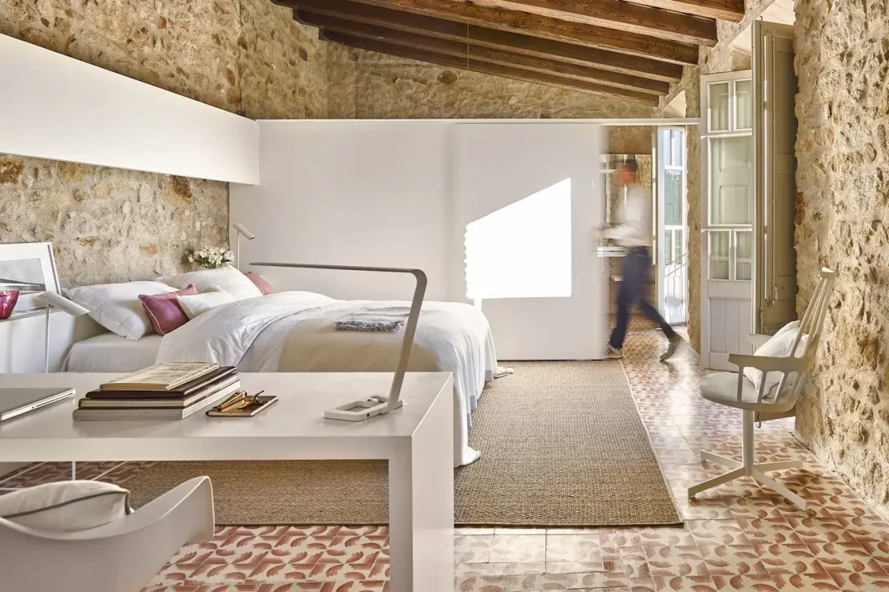 Habitación con cama, escritorio y una persona caminando. Usa paredes falsas para separar espacios, integrando piedra rústica y diseño moderno.