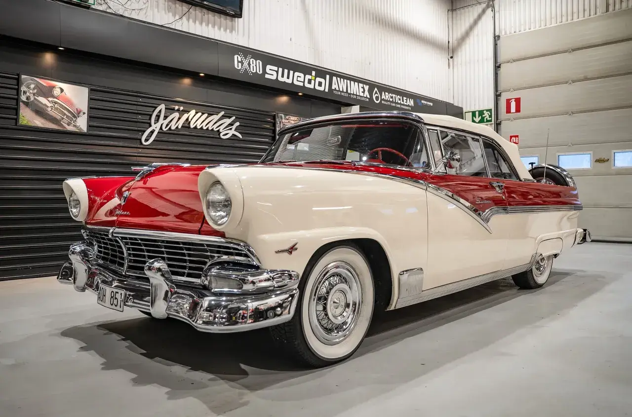 En skinande röd och vit Ford 56 cabriolet står i ett garage.