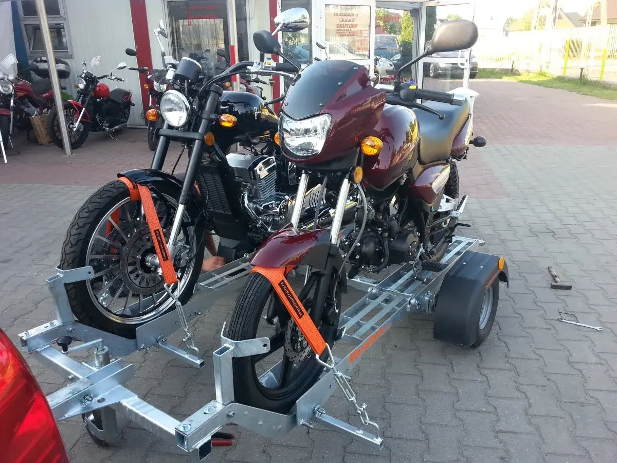 Dwa motocykle na przyczepie, zabezpieczone pasami.