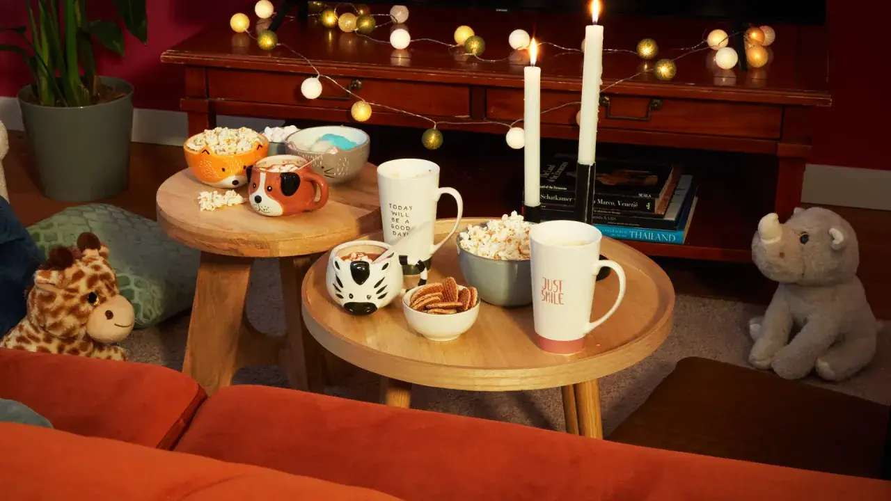 Tavolini bassi con tazze a tema animale, popcorn e biscotti, perfetti per una serata cinema a casa.