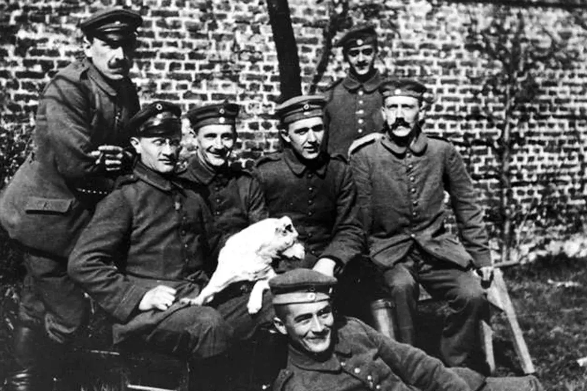 Grupp soldater i uniform, en håller en vit hund. En av männen liknar en ung Hitler.