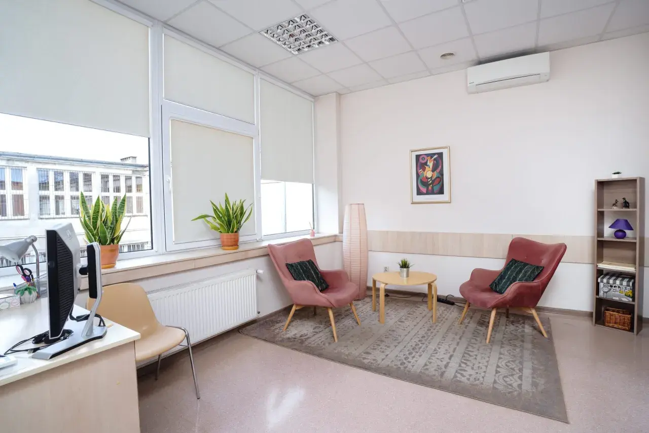 Jasne, przytulne wnętrze gabinetu psychologicznego z dwoma różowymi fotelami i stolikiem.