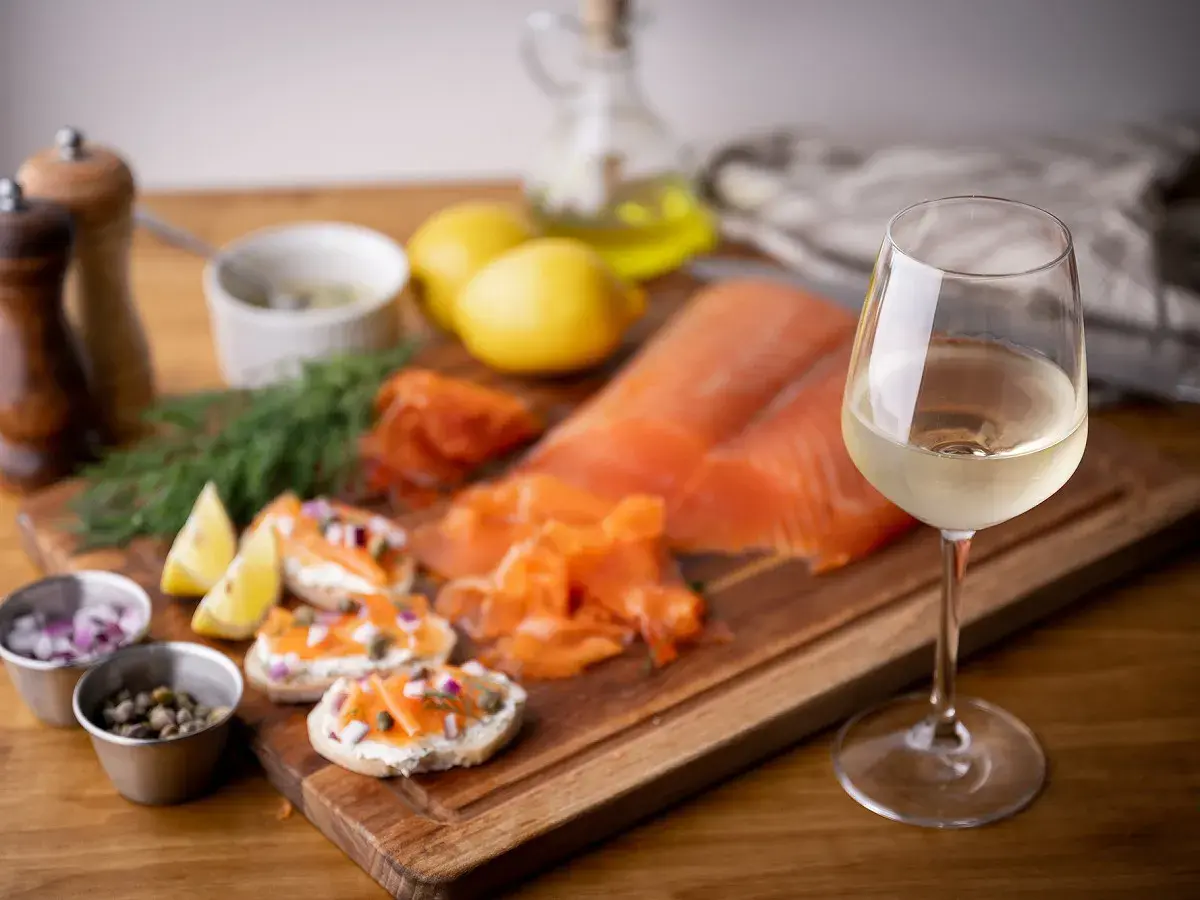 Un verre de vin blanc frais accompagne un saumon fumé et des toasts. Parfait pour savoir quel vin avec du saumon en papillote.