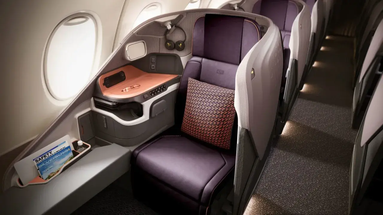 Luxuriöser Sitzbereich in der **besten Business Class** mit lila Ledersitzen, Kissen und einem Fenster.