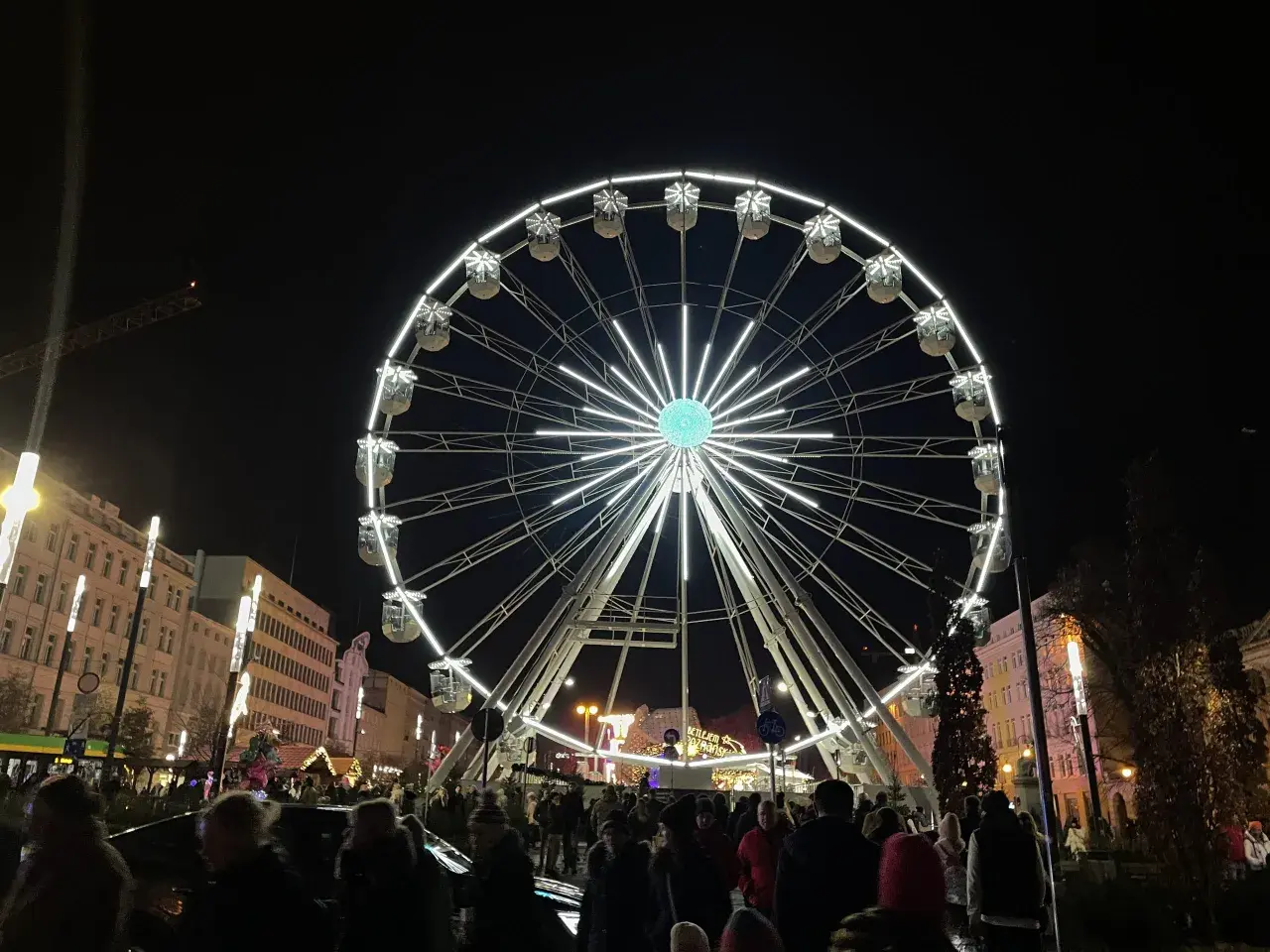 Nocny plac wolności poznań rozświetla ogromne koło widokowe. Tłumy ludzi spacerują wśród świątecznych iluminacji.