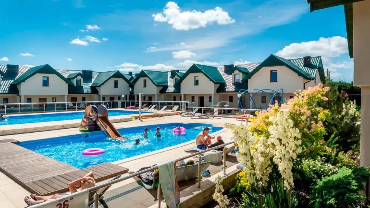 Rodzinny wypoczynek w domkach apartamentowych Fulay Premium. Dzieci bawią się w basenie ze zjeżdżalnią, dorośli relaksują się na leżakach.
