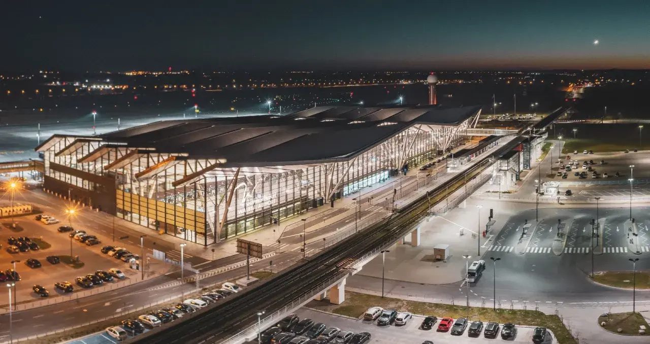 Nowoczesny terminal lotniska w Gdańsku nocą. Widok z góry pokazuje parkingi, drogi i tory kolejowe, ułatwiając planowanie, jak dojechać na lotnisko w Gdańsku.