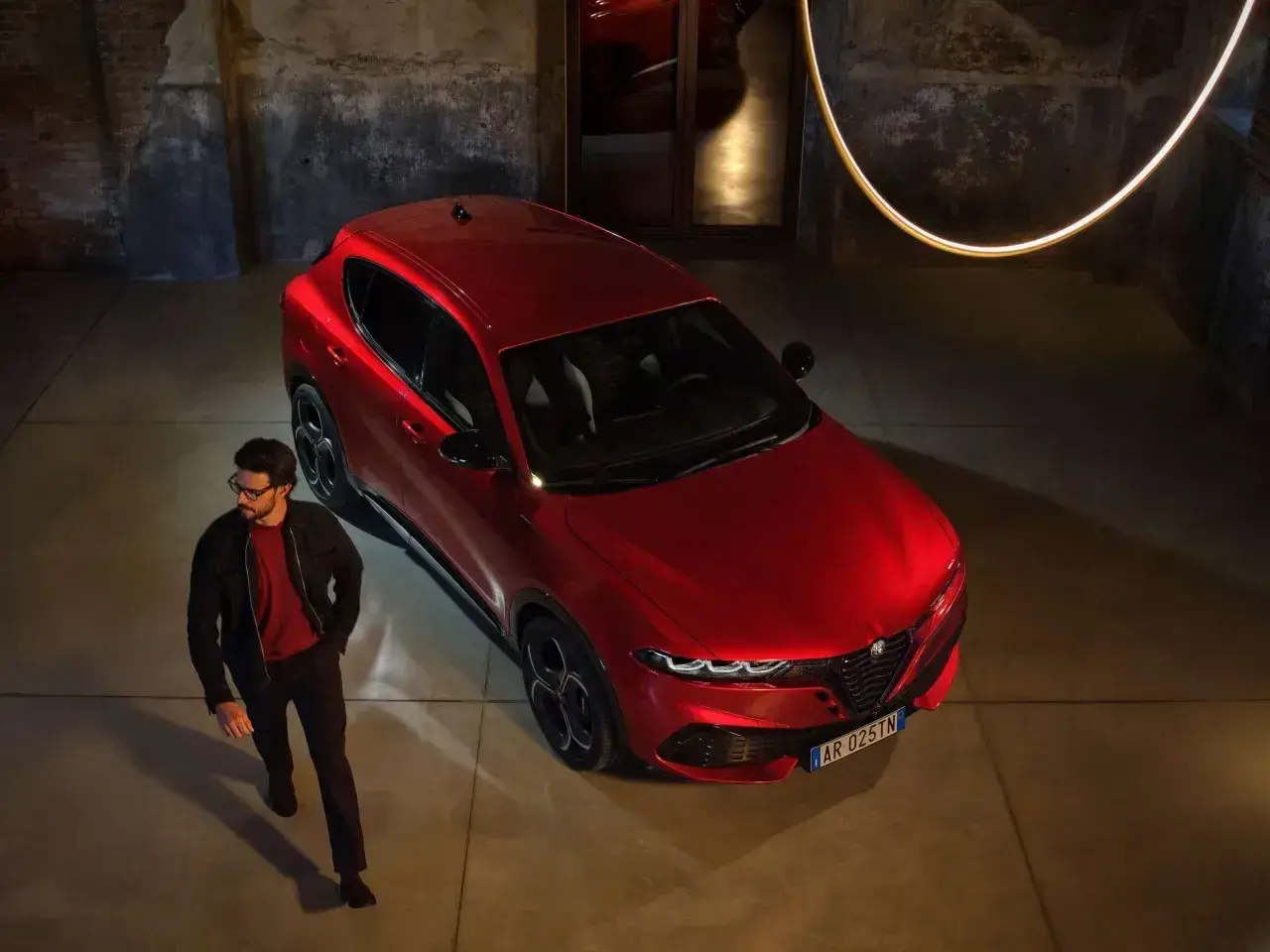 Elegancki mężczyzna obok czerwonego Alfa Romeo Tonale. Sprawdź aktualną alfa romeo tonale cena i odkryj jego styl.