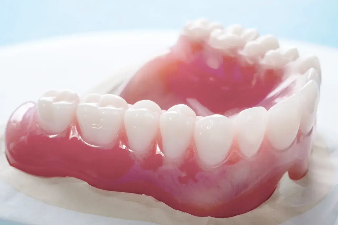 Un primo piano di una dentiera rosa con denti bianchi. La dentiera mi fa vomitare.