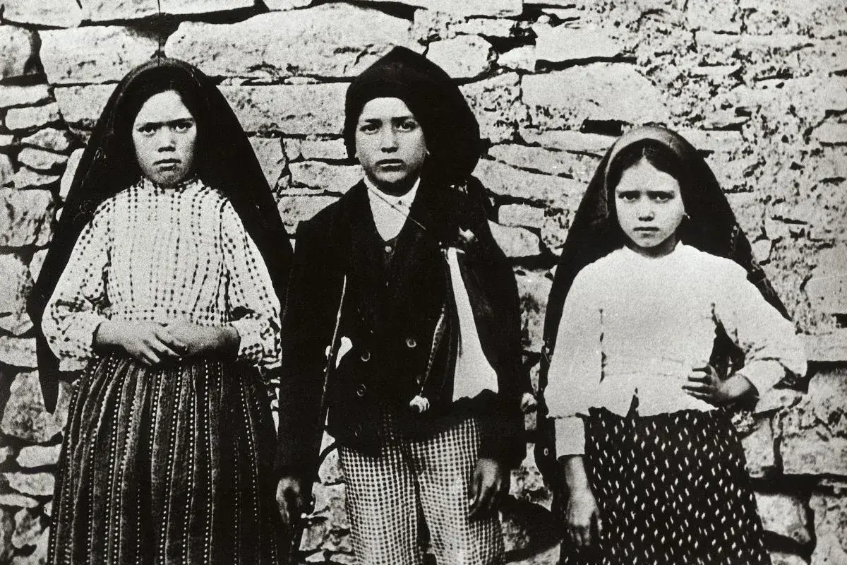 Trójka dzieci, w tym siostra Łucja z Fatimy, pozuje przed kamiennym murem.