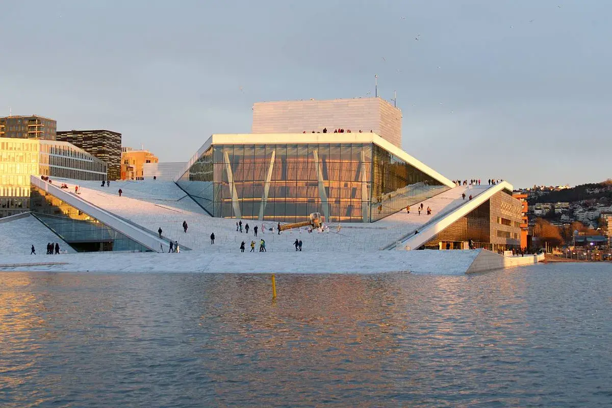 Oslo Winter: Menschen spazieren auf dem Dach der Oper, die im warmen Abendlicht glänzt.