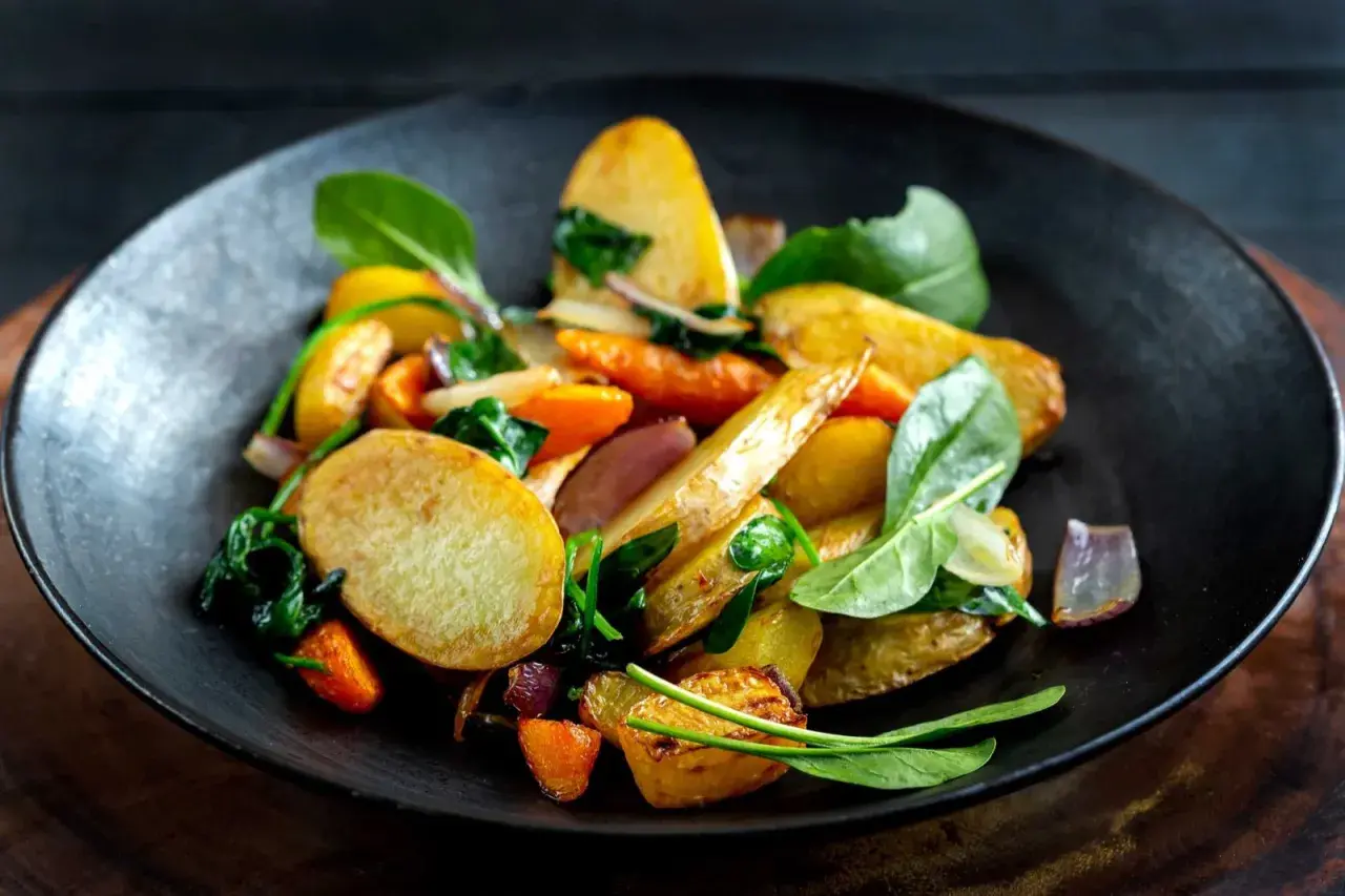 En tallrik med ugnsrostade rotfrukter, inklusive potatis, morötter och rödlök, blandat med färsk spenat. En härlig rotfrukter lista för en god måltid.
