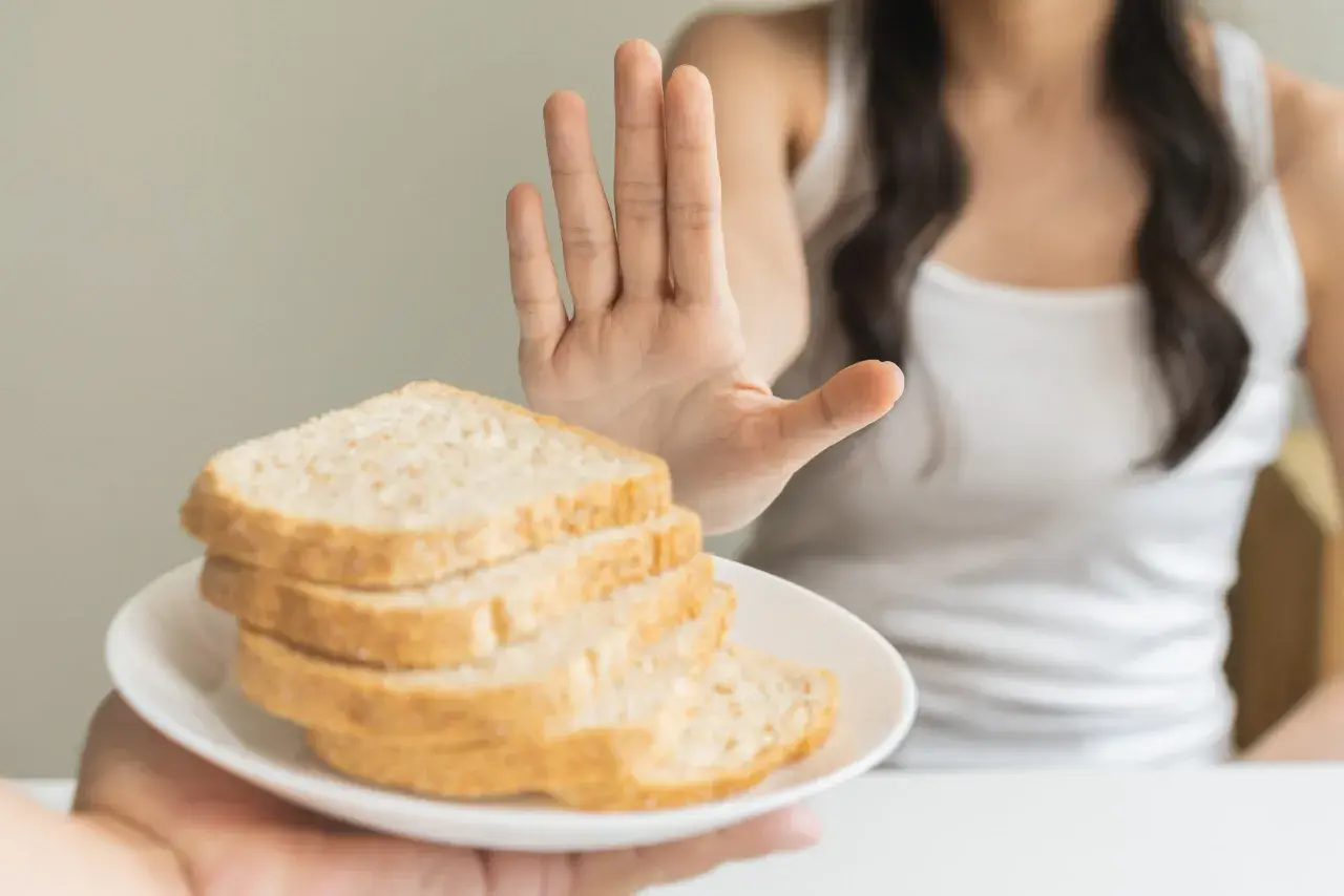 Osoba odrzuca talerz z chlebem, pokazując dłoń. To symbol walki z celiakią i unikania glutenu.