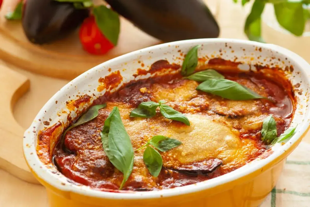 Aubergine parmigiana dorée et gratinée, garnie de feuilles de basilic frais. Un plat réconfortant prêt à être dégusté.