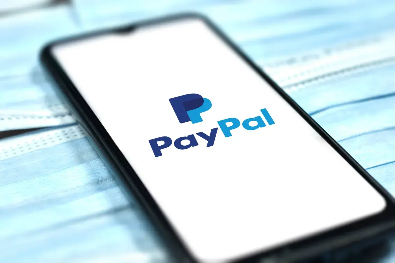 Smartfon z logo PayPal na ekranie, leżący na niebieskich maseczkach ochronnych. Szybkie i bezpieczne płatności online.