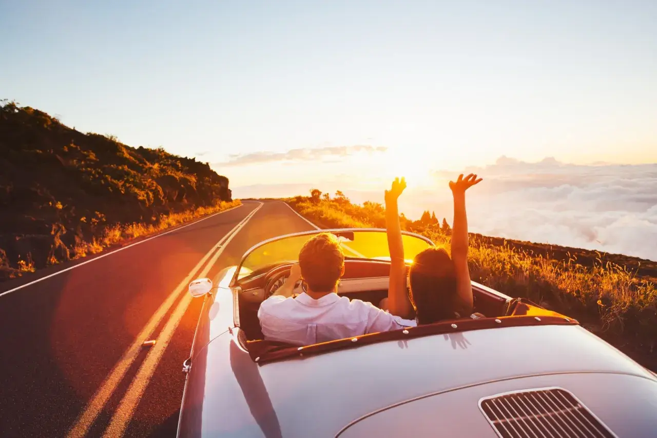 Coppia in auto decappottabile al tramonto, con le braccia alzate, godendosi un itinerario Croazia da sogno.