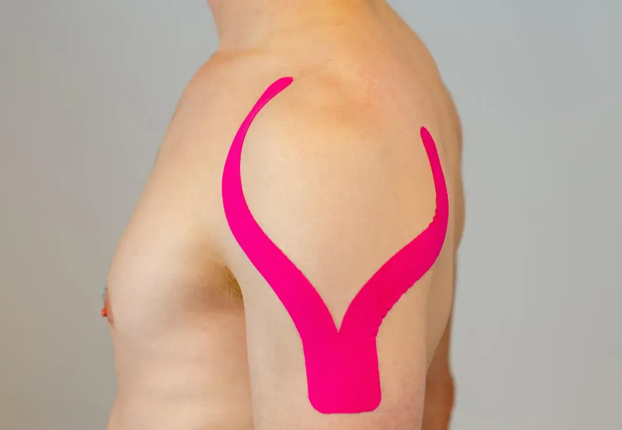 Schulter tapen: Ein Mann mit pinkem Kinesio-Tape auf der Schulter, das wie ein aufgeschlagenes Buch aussieht.