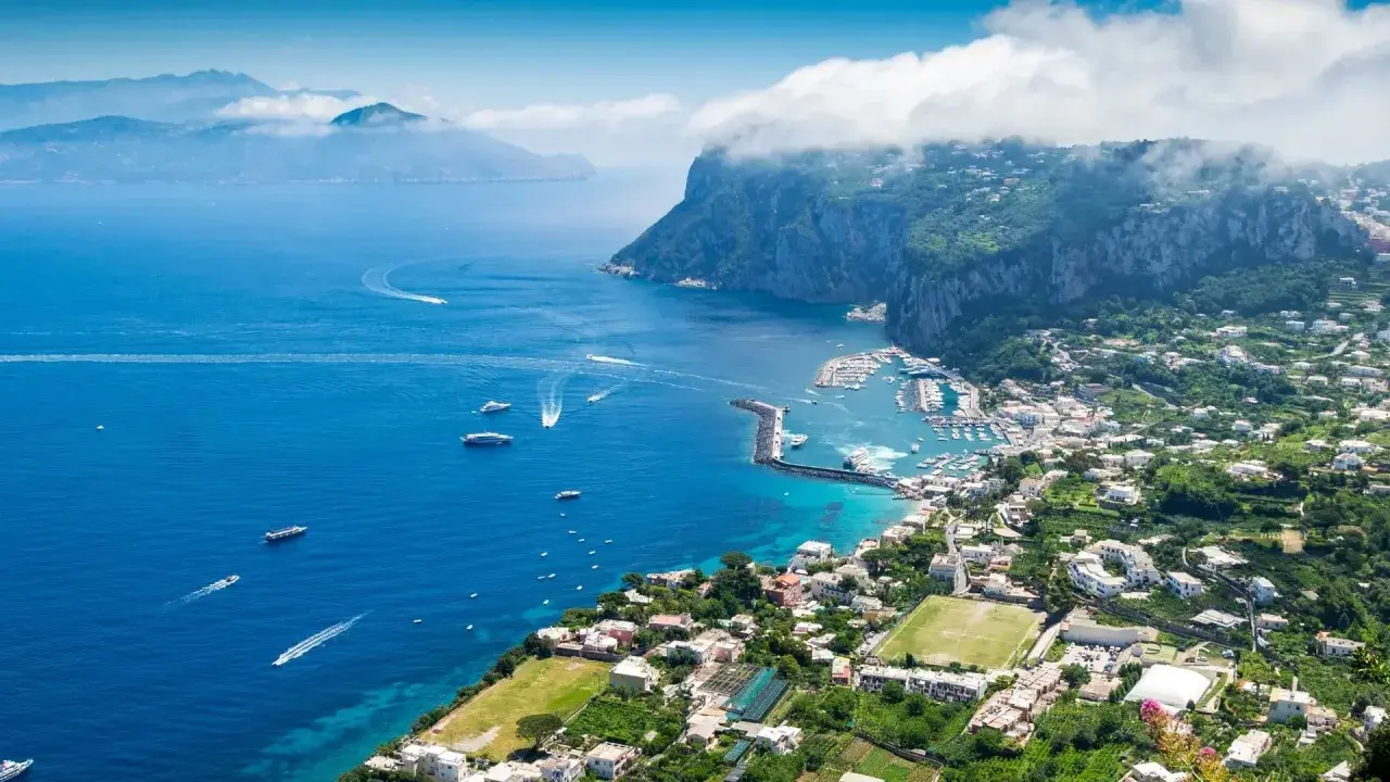 Widok na zatokę z łodziami i miasteczkiem na zboczu góry Capri.