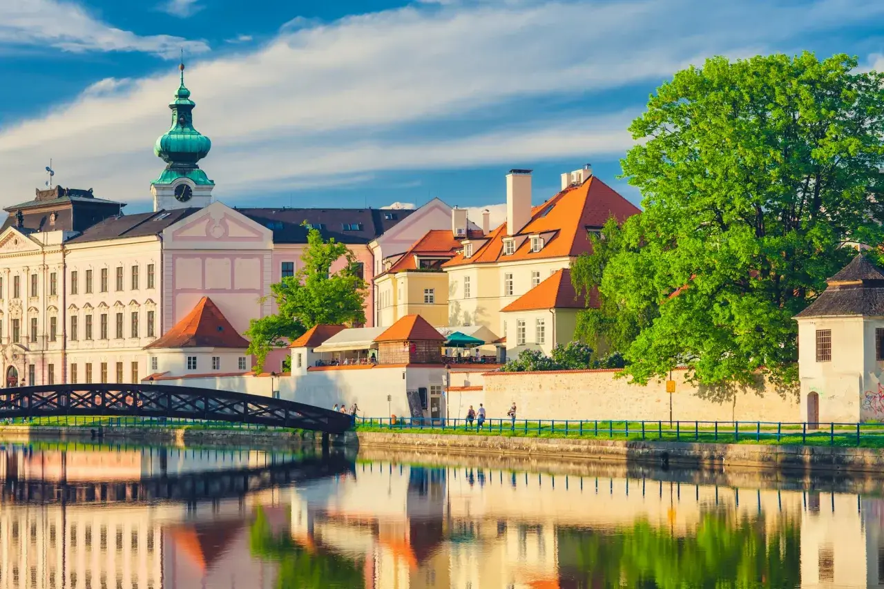Idyllische Stadtansicht in Südböhmen mit Spiegelungen im Wasser. Ein eleganter Bogenbrücke führt zu bunten Häusern mit roten Dächern.