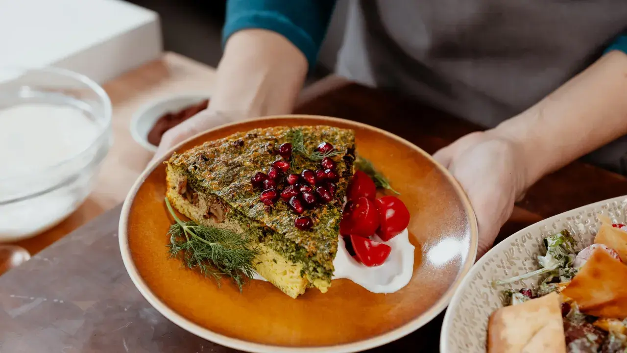 Une part de kuku sabzi, une tarte aux herbes persane, garnie de grenades et de tomates cerises, servie avec une touche de yaourt.