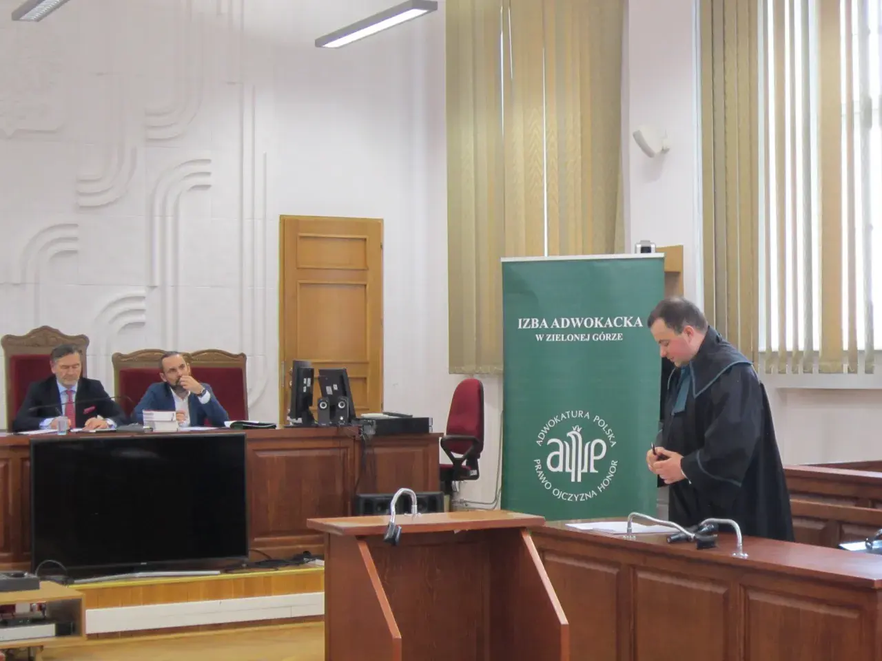 Sąd w Zielonej Górze: dwaj mężczyźni w togach siedzą za stołem, jeden w todze stoi obok.