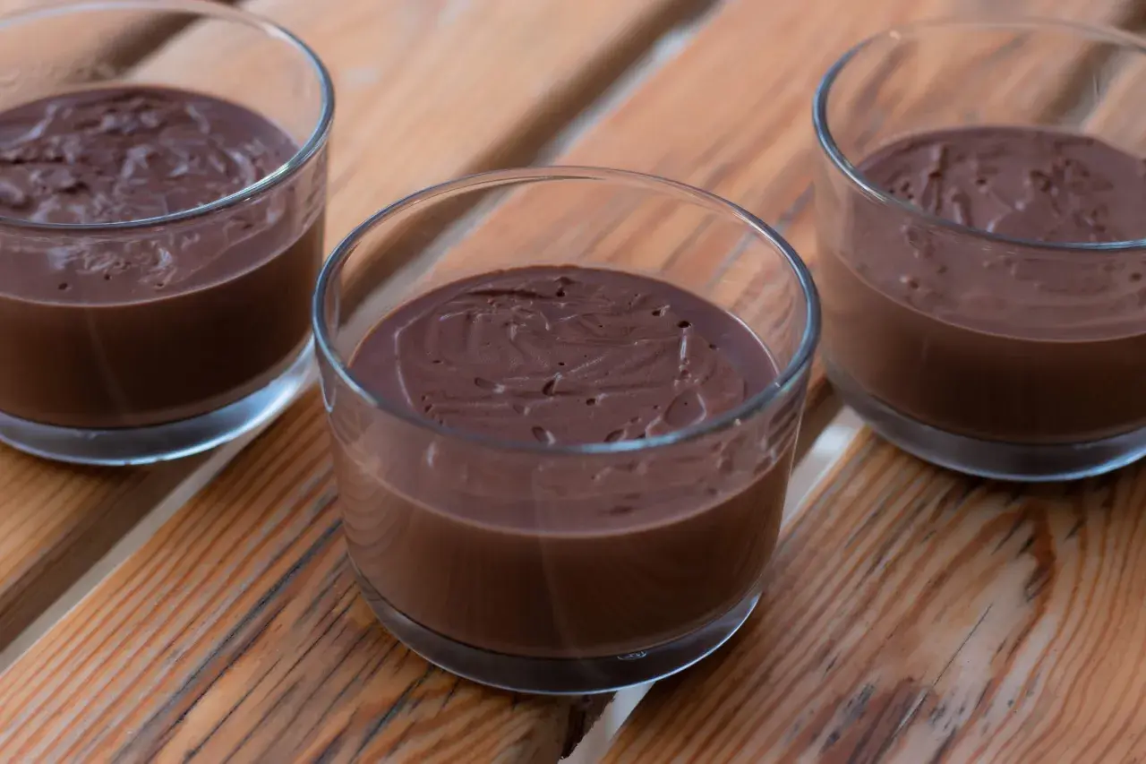 Tre glas med krämig, hemmagjord chokladpudding står på en träyta.