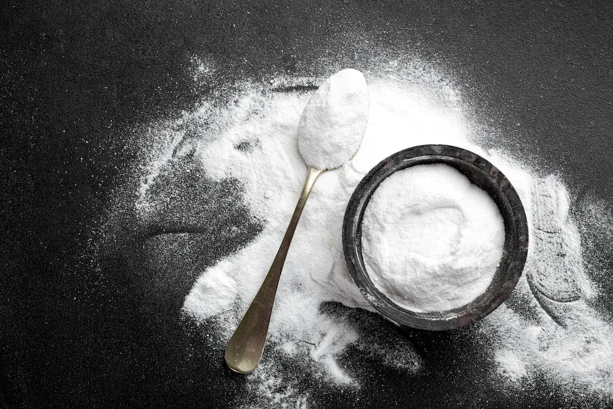 Un cucchiaio e una ciotola pieni di carbonato di sodio, mostrando i suoi molteplici usi in cucina e per la pulizia.