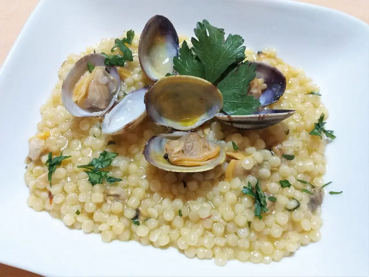 Piatto di fregola con vongole, profumata al prezzemolo e condita con un filo d'olio. Un classico della cucina sarda.