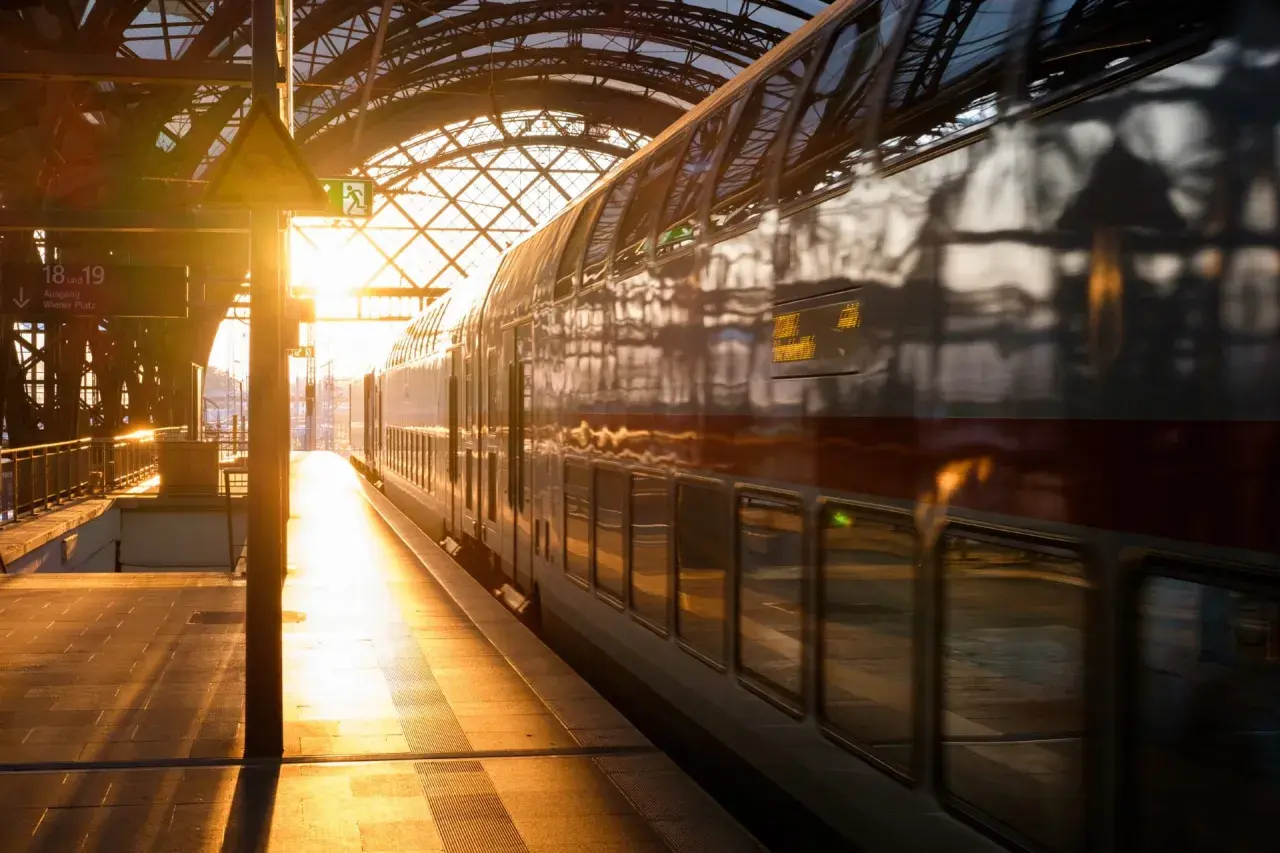 Złote światło wschodu słońca oświetla peron i pociąg PKP. Widok na dworzec kolejowy z pociągiem dwupoziomowym.