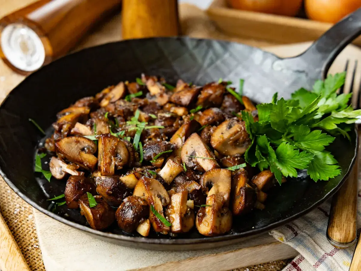Gebratene Champignons in einer Pfanne, garniert mit Petersilie. Köstlich und einfach zuzubereiten.