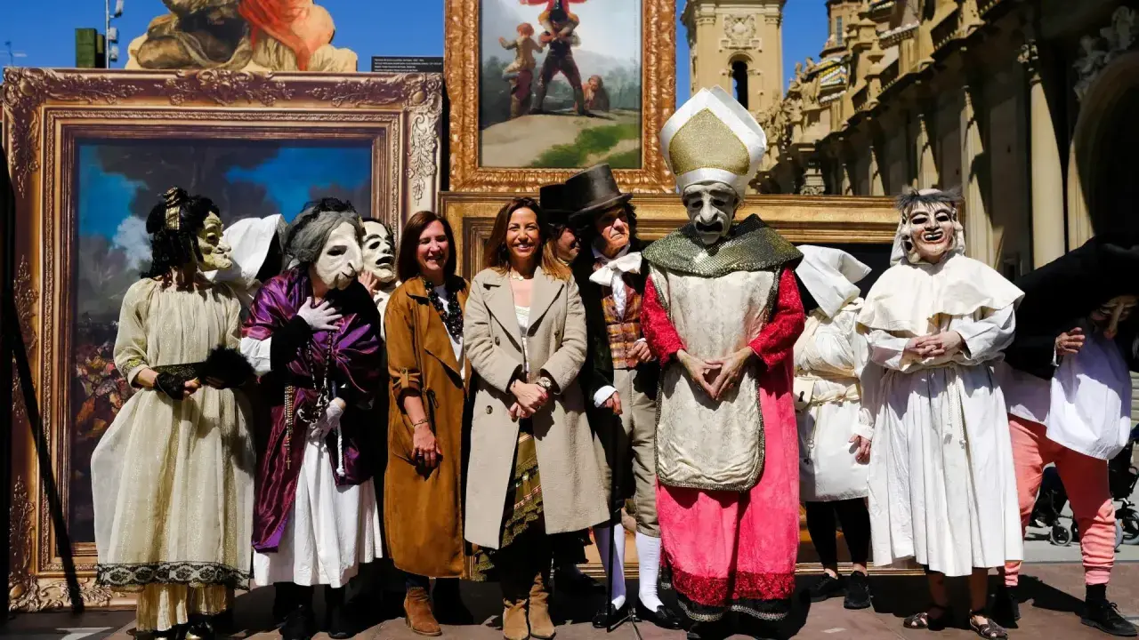 Personas enmascaradas y vestidas con trajes de época posan frente a cuadros, recreando el espíritu de las fiestas goyescas.