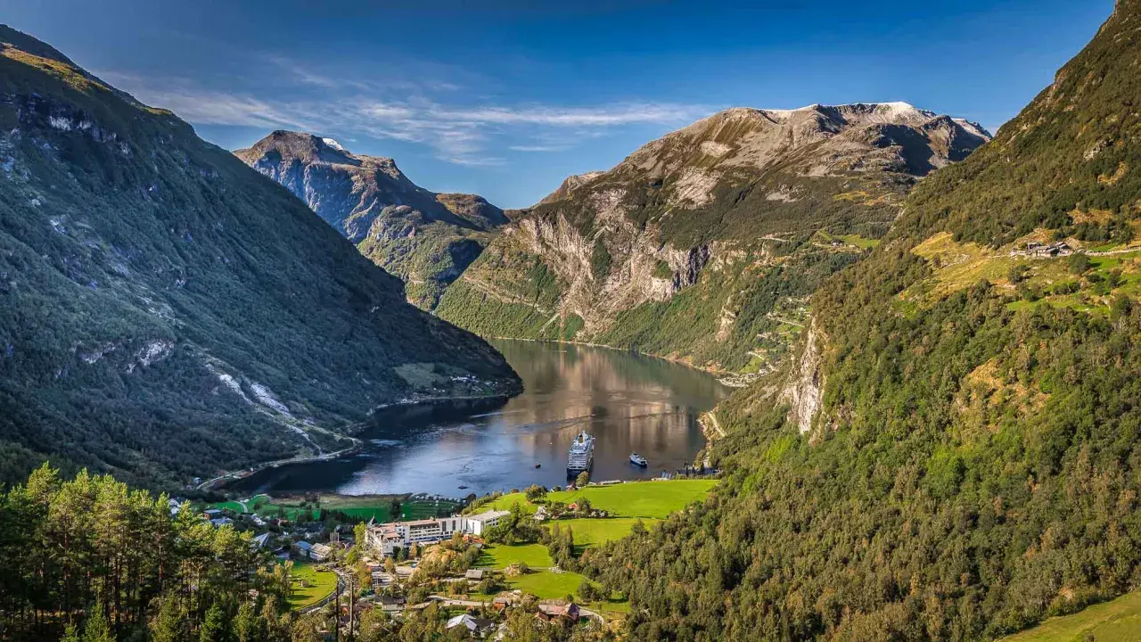 Majestätische fjorde norwegen, mit einem Kreuzfahrtschiff auf dem ruhigen Wasser, umgeben von steilen, grünen Bergen und einem kleinen Dorf.