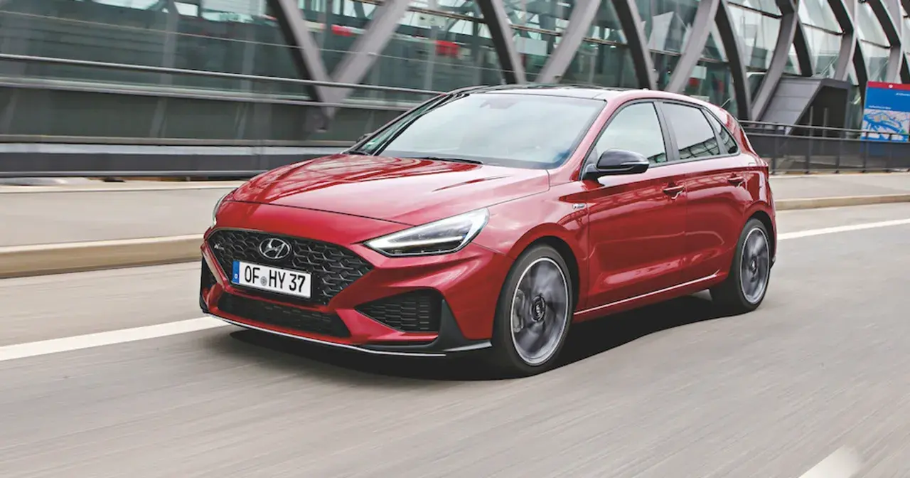 Czerwony Hyundai i30 2024 w wersji N Line pędzi po drodze, z nowoczesną atrapą chłodnicy i ostrymi światłami LED.