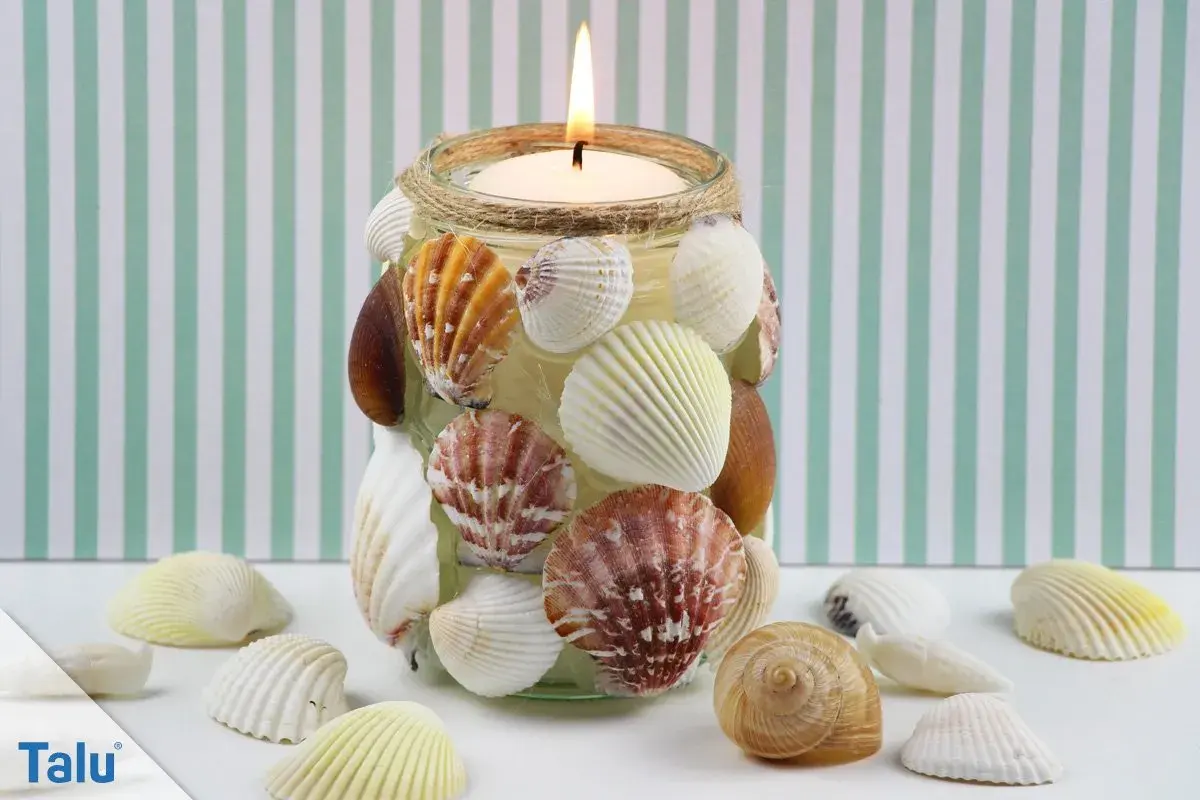 Kerzenglas mit Muscheln verziert, ein schönes Beispiel für basteln mit Muscheln. Ein warmes Licht scheint durch die maritime Dekoration.