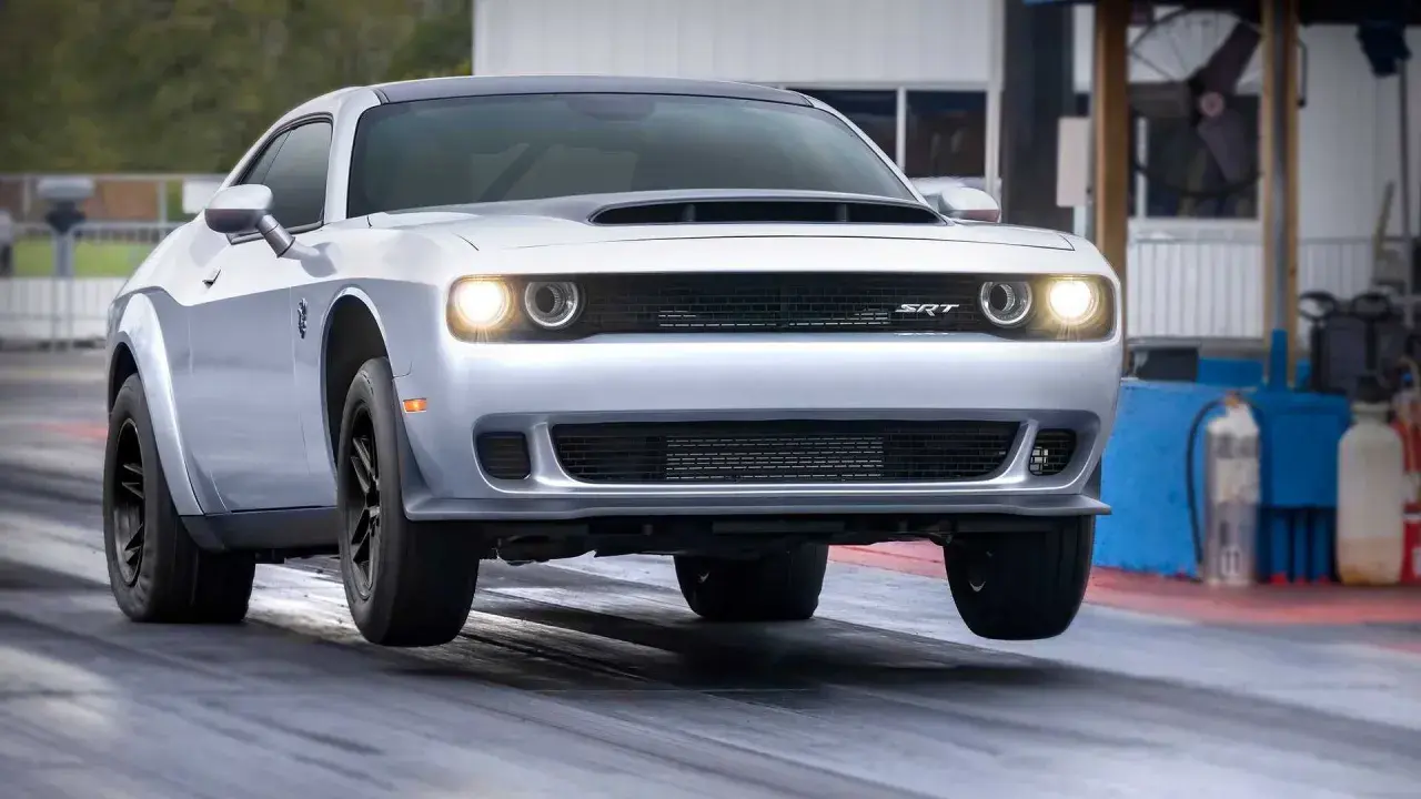 Srebrny Dodge Challenger SRT na torze wyścigowym, z przednimi kołami lekko uniesionymi nad asfaltem.
