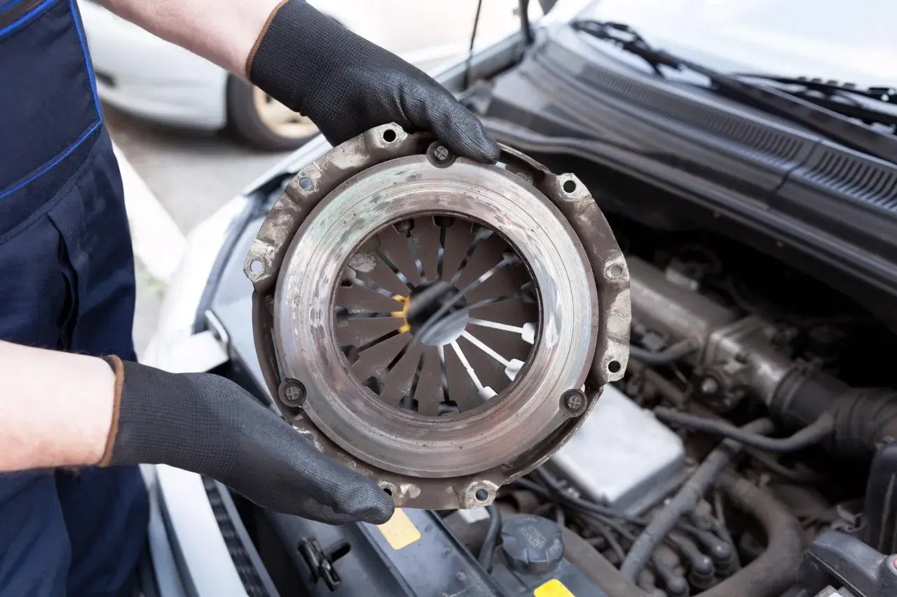 Mechanic holding a car clutch assembly with engine in background.
