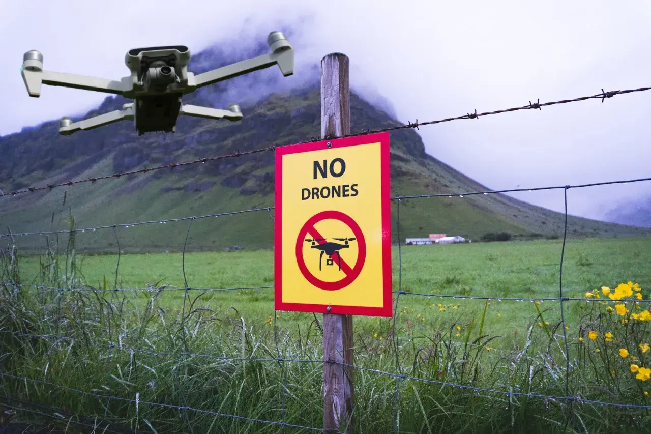 Un drone vola vicino a un cartello "Vietato l'utilizzo drone" in un paesaggio rurale nebbioso.