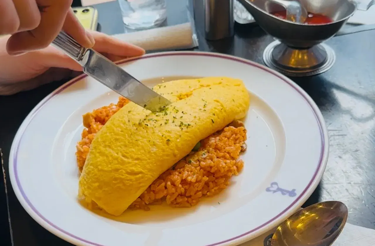 A knife cuts into a fluffy omelet atop rice, a delicious example of Japanese dishes with cheese.
