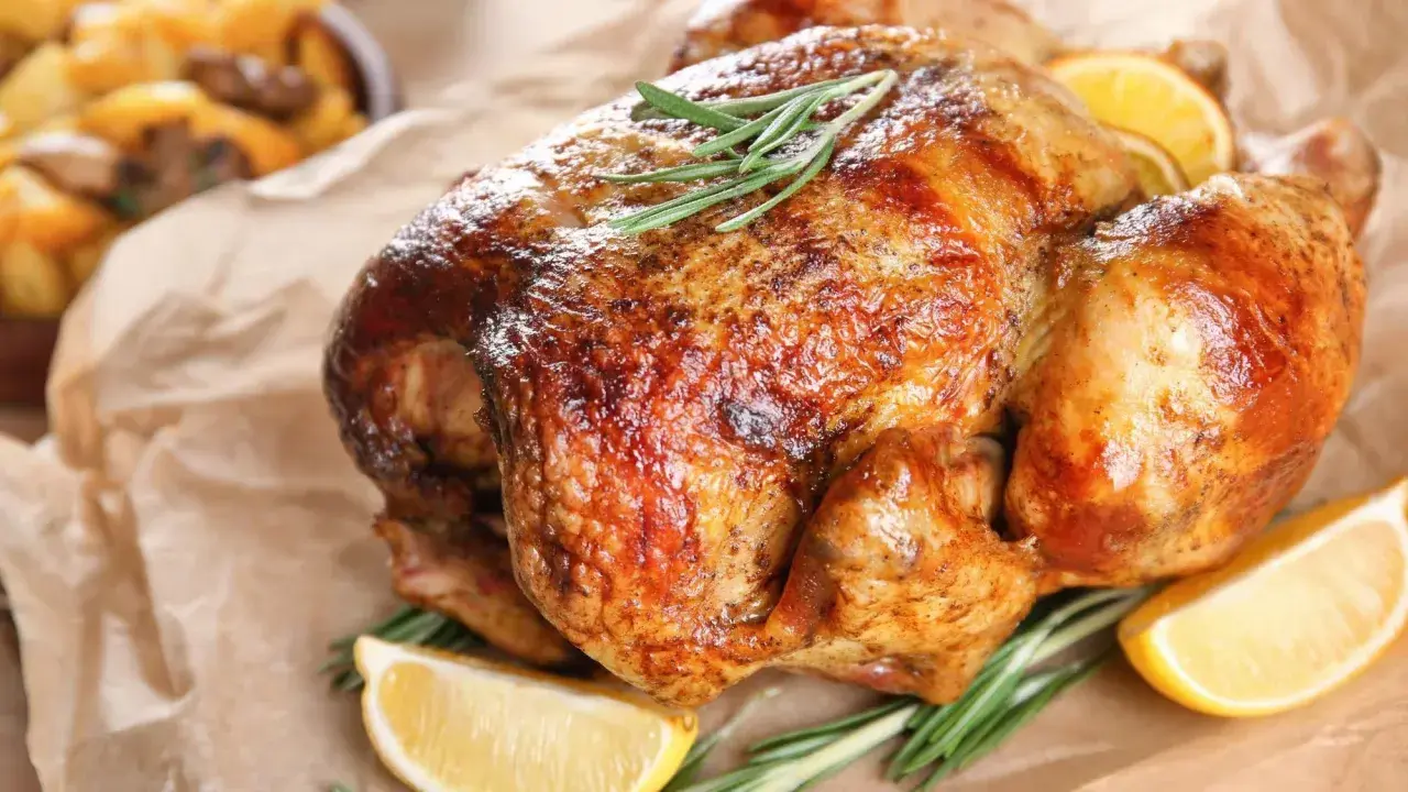 Un poulet rôti doré, garni de romarin et de quartiers de citron, prêt à être dégusté après une cuisson parfaite à 150 degrés.