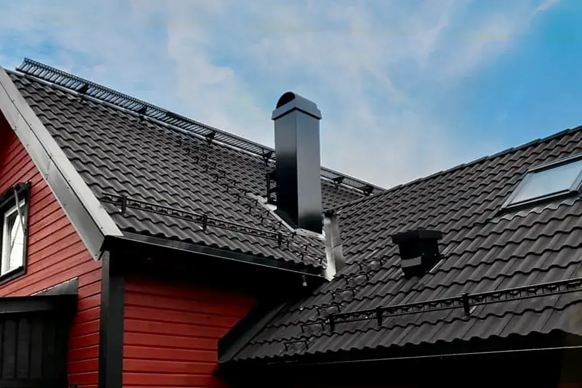 Svart, modern skorsten på ett tak med mörka takpannor. En röd träfasad syns till vänster.
