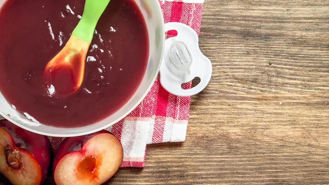 Schüssel mit pflaumenmus baby, Löffel, Schnuller und frische Pflaumen auf Holztisch.