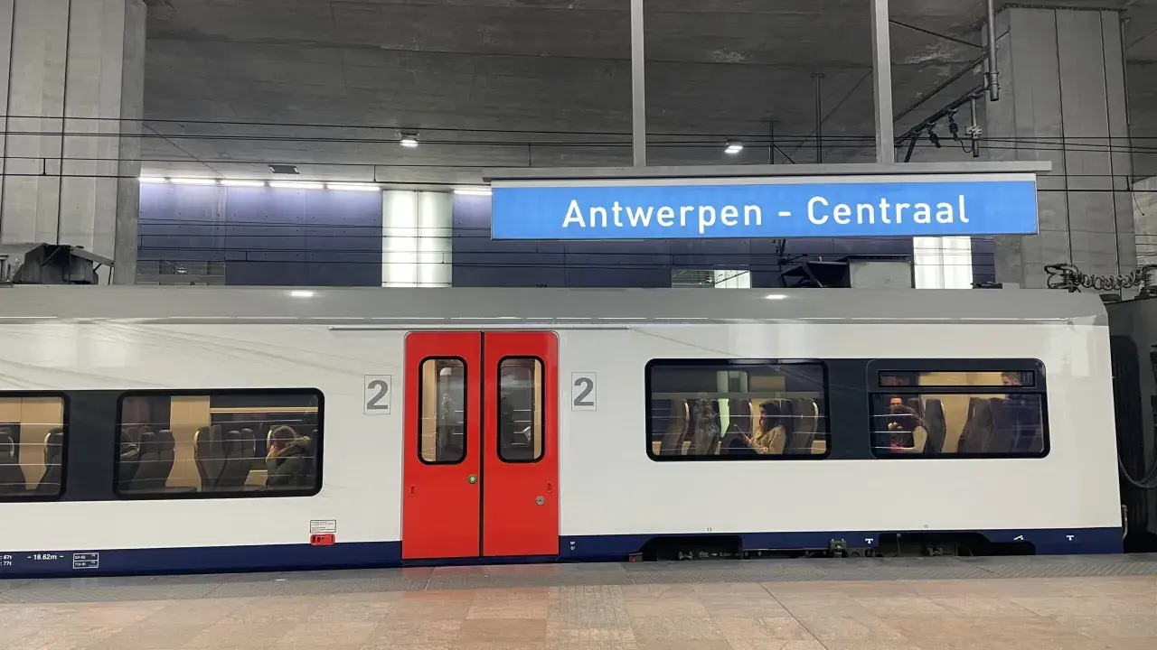 Pociągiem po Europie: biały wagon z czerwonymi drzwiami na stacji Antwerpen - Centraal. W oknach widać pasażerów.