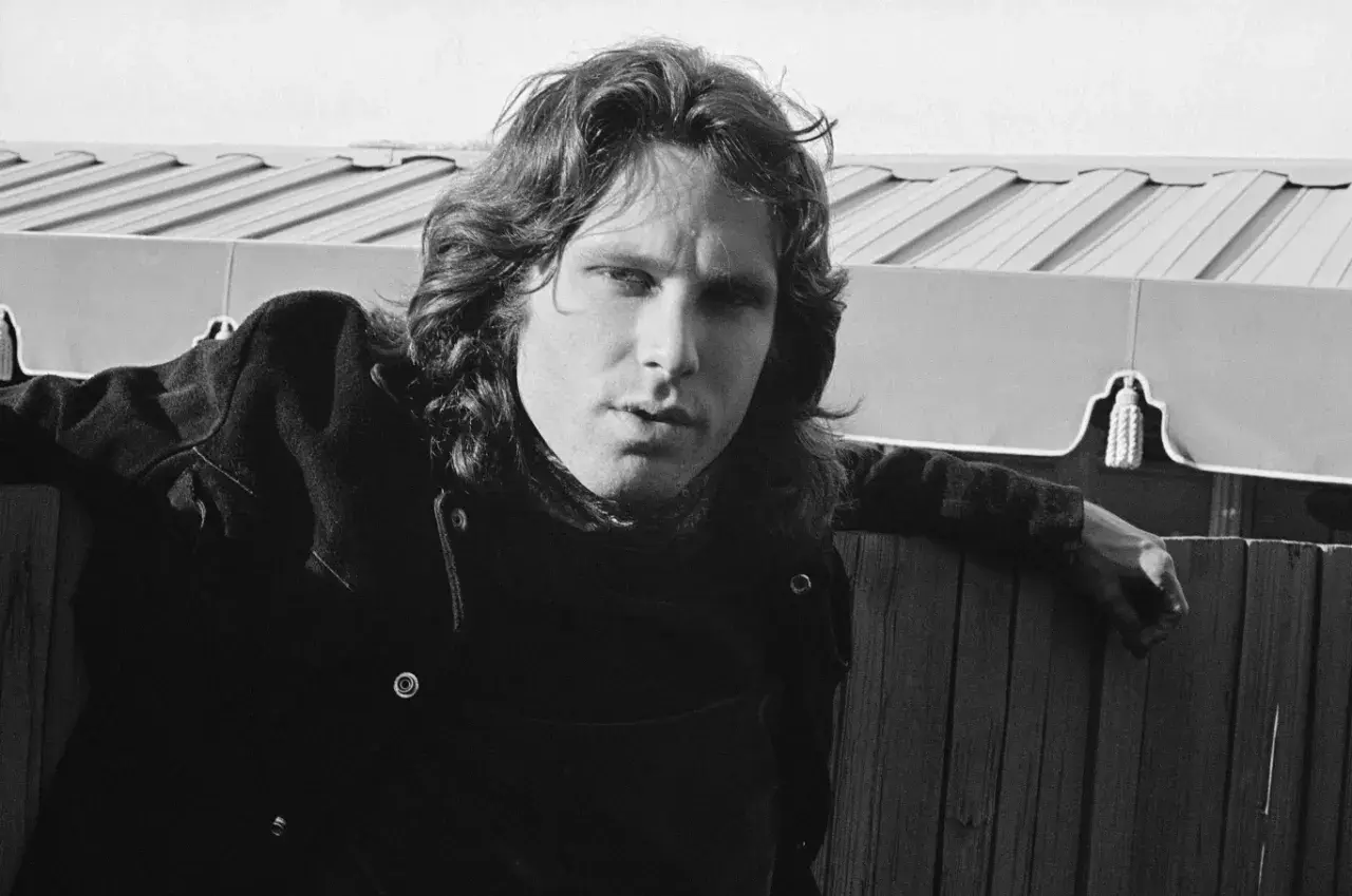 Jim Morrison, wokalista The Doors, oparty o drewniany płot, zamyślony.