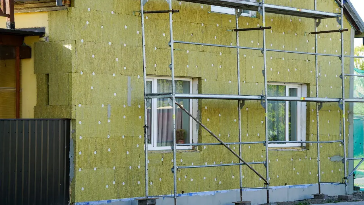 Dom ocieplany najlepszą wełną mineralną. Widać rusztowanie i okna.