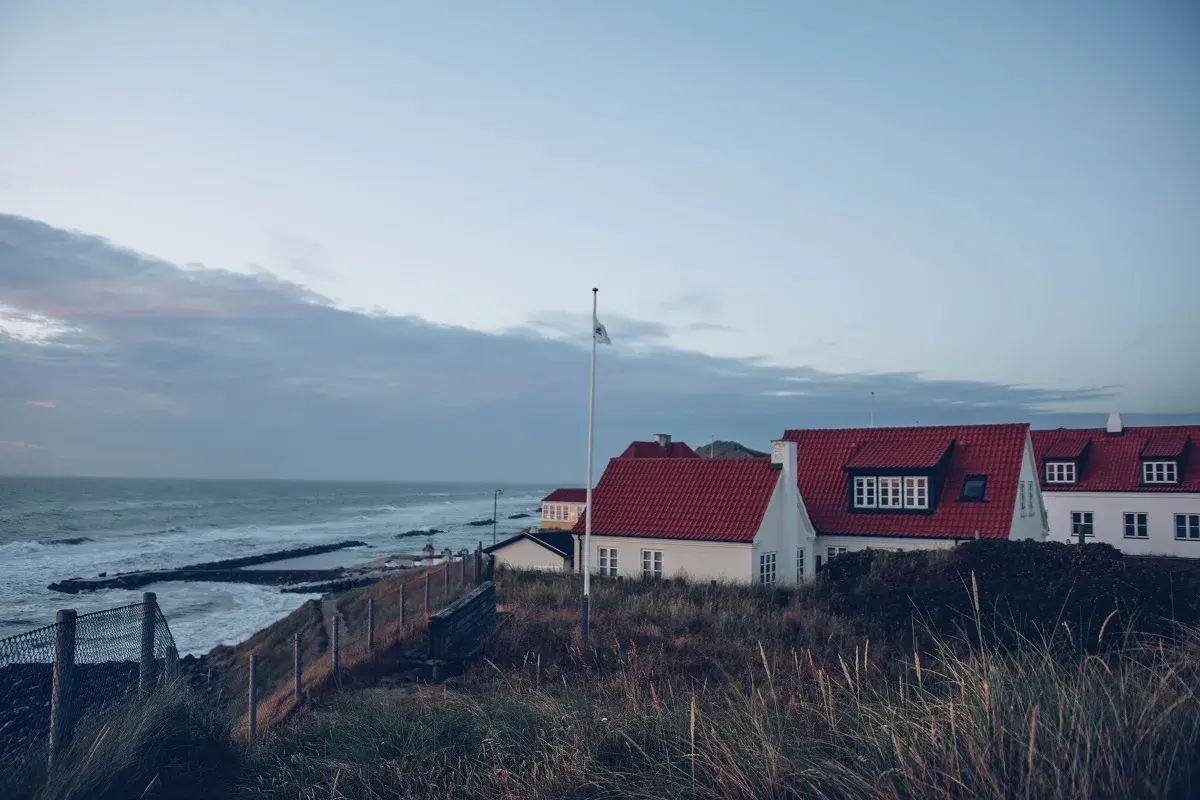 Vackra vita hus med röda tak vid havet, perfekt för en **weekendresa Danmark**. Gräs och staket i förgrunden.
