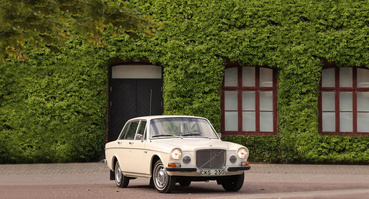 En klassisk Volvo 164 från 1973 parkerad framför en vackert klätterväxttäckt byggnad.