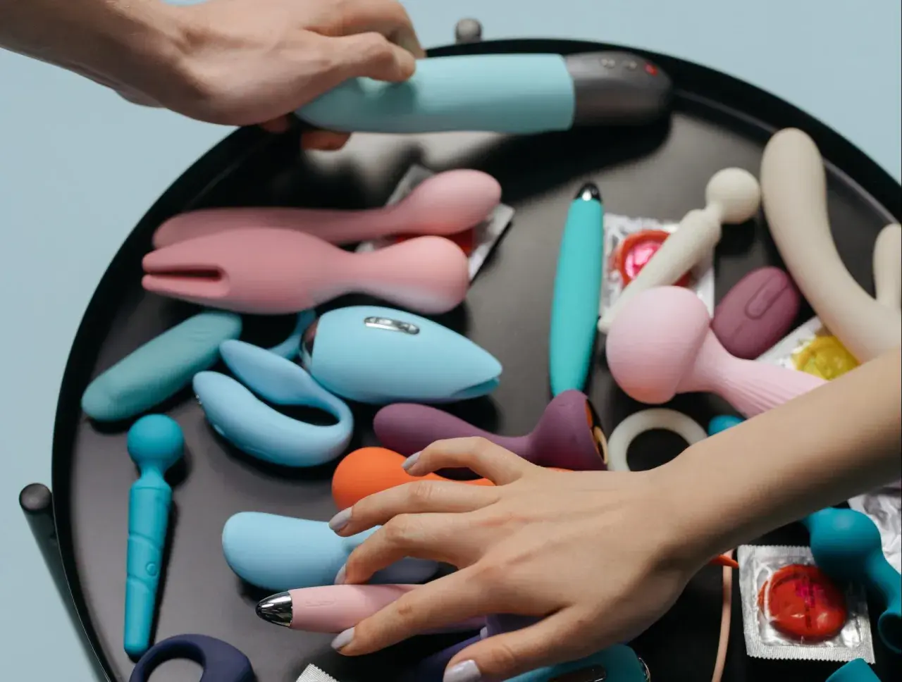 Mani che scelgono tra vari vibratori e sex toys, suggerendo la masturbazione femminile.