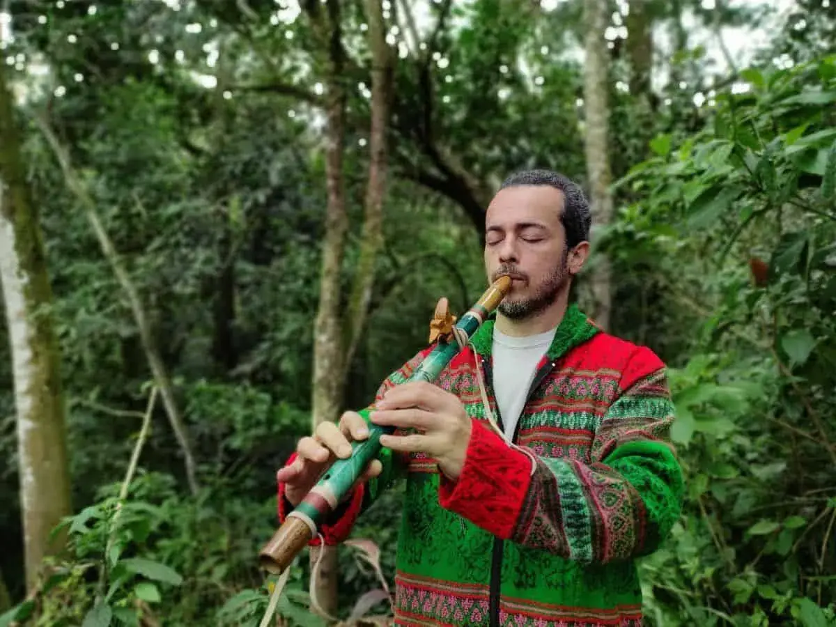 Un homme joue d'un instrument de musique à bec coloré dans une forêt luxuriante.
